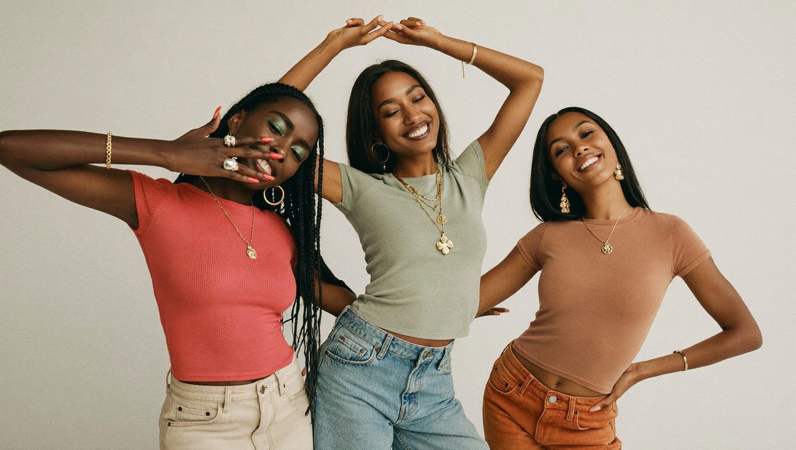 Três modelos sorrindo em estúdio, de baby look rosa, verde e terracota com jeans